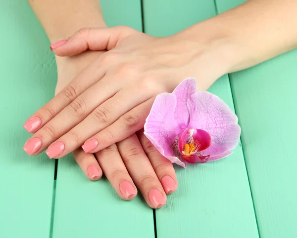 Kobieta ręce z różowy manicure i orchidea na kolor drewniane tła — Zdjęcie stockowe