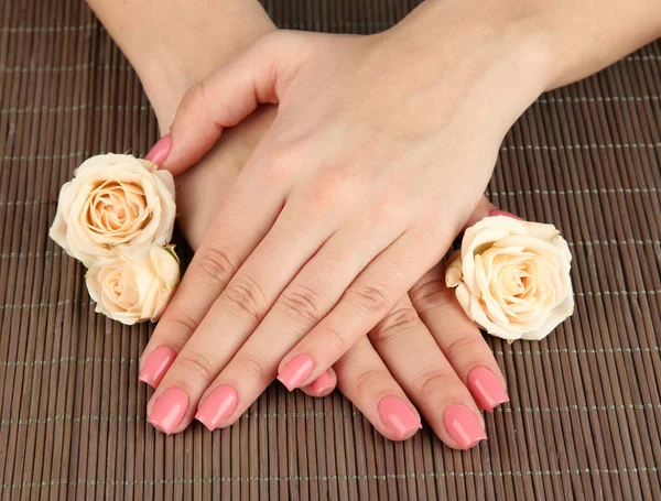 Mãos de mulher com manicure rosa e flores, em fundo tapete de bambu — Fotografia de Stock