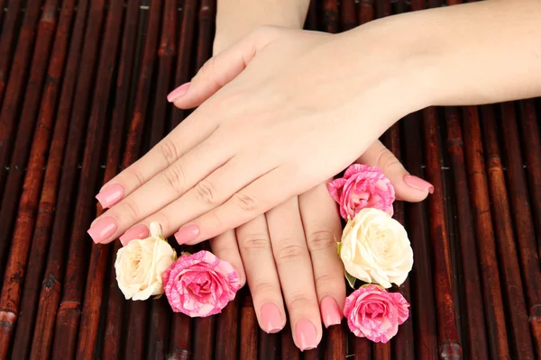 Mãos de mulher com manicure rosa e flores, em fundo tapete de bambu — Fotografia de Stock