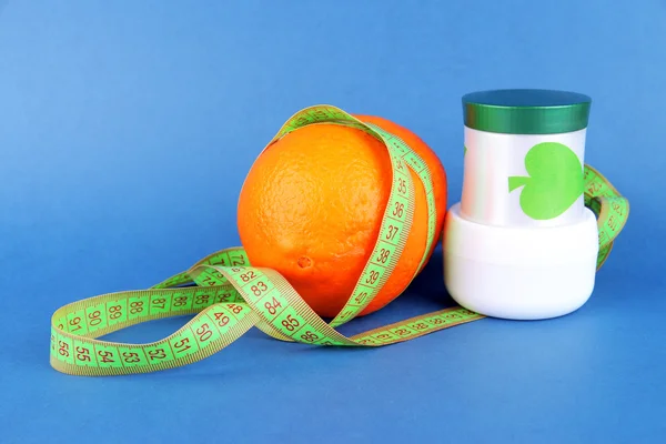 Orange with measuring tape and body cream, on color background — Stock Photo, Image