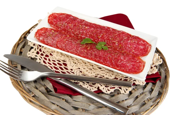 Tasty salami on plate on wicker cradle isolated on white — Stock Photo, Image