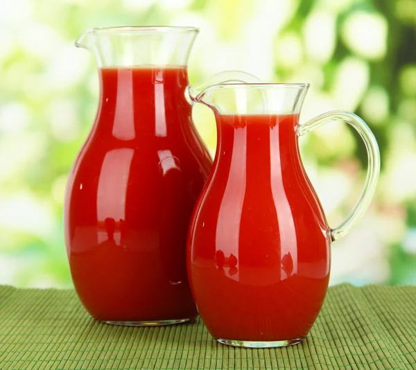 Tomatensaft in Krügen auf Tisch vor hellem Hintergrund — Stockfoto