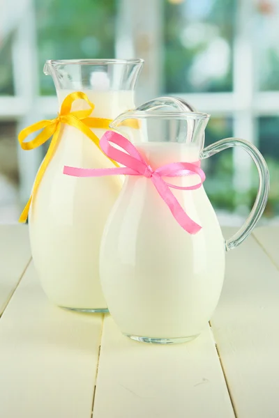 Pitchers of milk on table in room — Stock Photo, Image