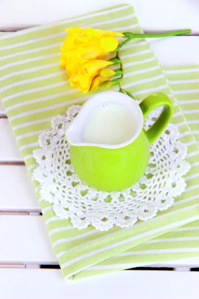 Zelený džbánek s mlékem na ubrousek na dřevěný piknikový stůl detail — Stock fotografie