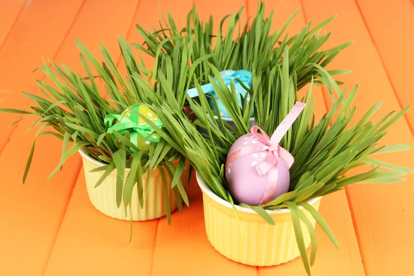 Velikonoční vejce v miskách s trávou na oranžové dřevěný stůl zblízka — Stock fotografie
