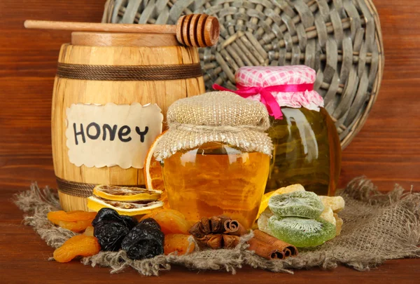 Jars of honey, wooden barrel, drizzler and dried fruits on wooden background — Stock Photo, Image