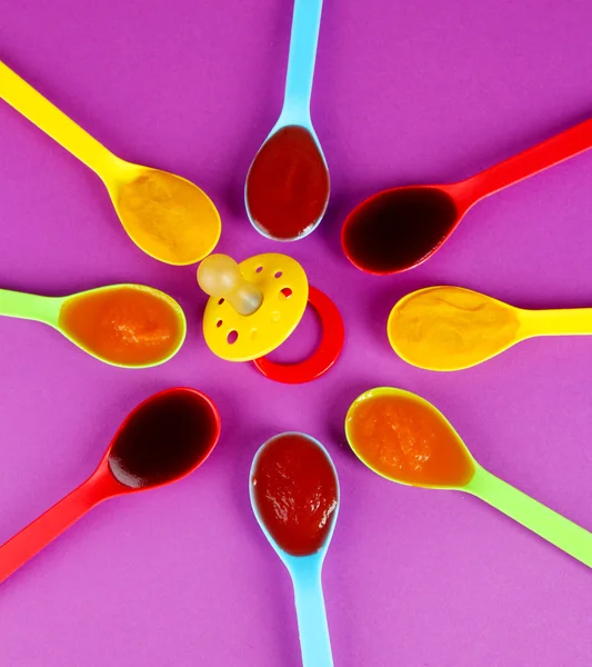 Baby puree in spoons with nipple on purple background — Stock Photo, Image