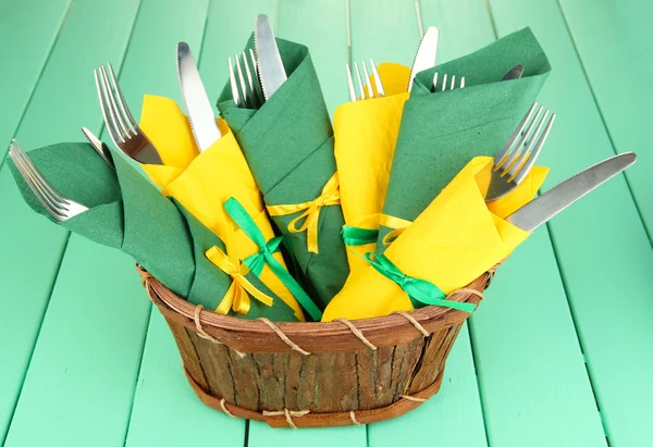 Çatal ve bıçaklar renk ahşap zemin üzerine yeşil ve sarı kağıt peçete sarılmış — Stok fotoğraf