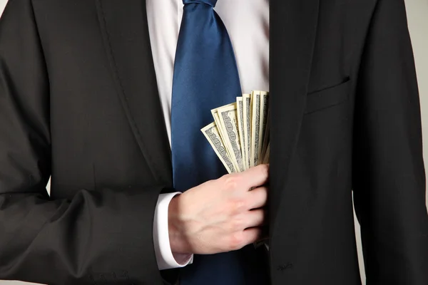 Business man hiding money in pocket on grey background — Stock Photo, Image