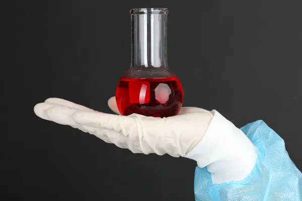 Стеклянная трубка с жидкостью в руке ученого во время медицинских испытаний на черном фоне — стоковое фото