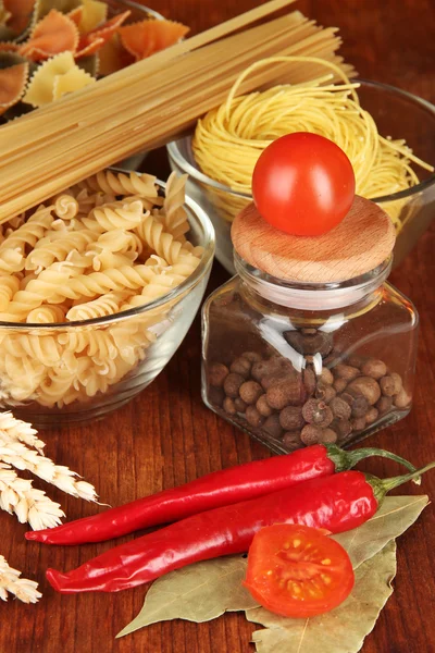 Olika typer av pasta, kryddor, tomater på ett träbord — Stockfoto