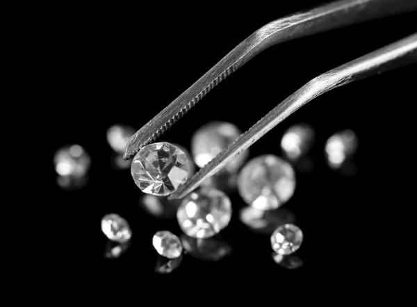 Prachtige schijnende kristallen (diamant) in het pincet, op zwarte achtergrond — Stockfoto