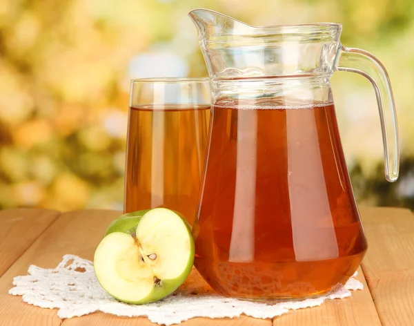 Fullt glas och kanna av äppeljuice och äpplen på träbord utomhus — Stockfoto