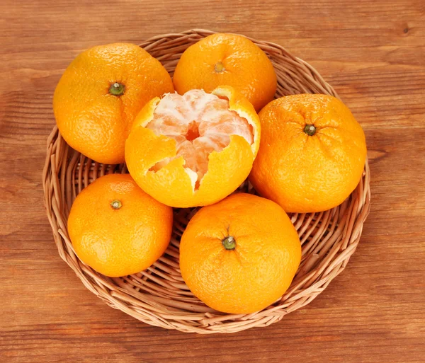 Tasty mandarines on wicker mat on wooden background — Stock Photo, Image
