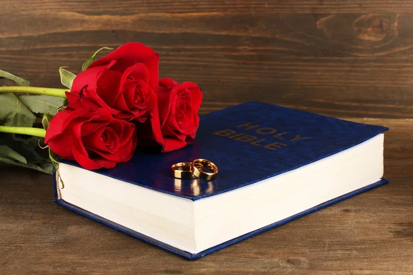 Wedding rings on bible with roses on wooden background — Stock Photo, Image