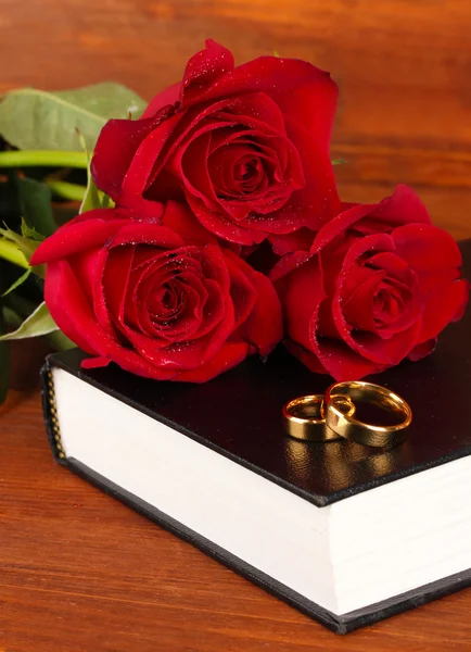 Обручальные кольца на библии с розами на деревянном фоне — стоковое фото