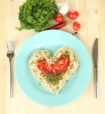 Cooked spaghetti carefully arranged in heart shape and topped with tomato sauce, on wooden background