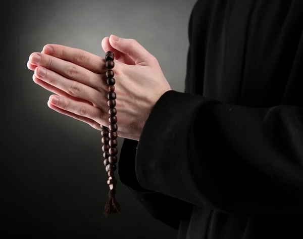 Sacerdote sosteniendo rosario, sobre fondo negro — Foto de Stock