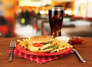 Tasty cheeseburger with fried potatoes and cold drink, on bright background clipart