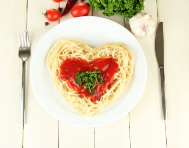 Cooked spaghetti carefully arranged in heart shape and topped with tomato sauce, on wooden background