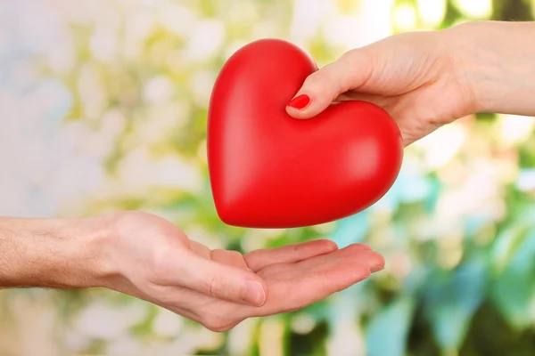 Corazón rojo en manos de hombre y mujer, sobre fondo verde — Foto de Stock