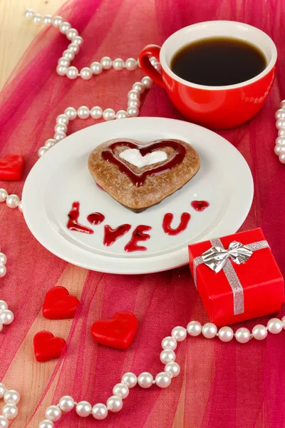 Chocolate cookie in form of heart with cup of coffee on pink tablecloth close-up — Stock Photo, Image