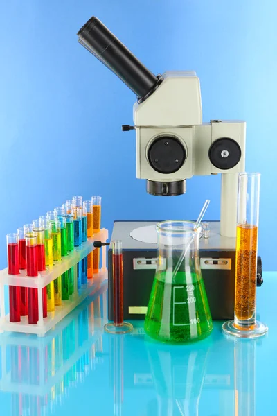 Test tubes with colorful liquids and microscope on blue background — Stock Photo, Image