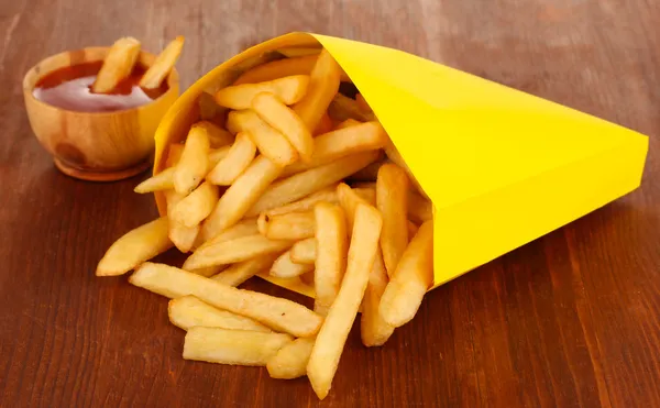 Papas fritas en bolsa de papel sobre mesa de madera de cerca — Foto de Stock