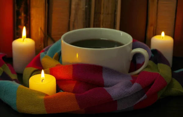 Cup of coffee wrapped in scarf on books background — Stock Photo, Image