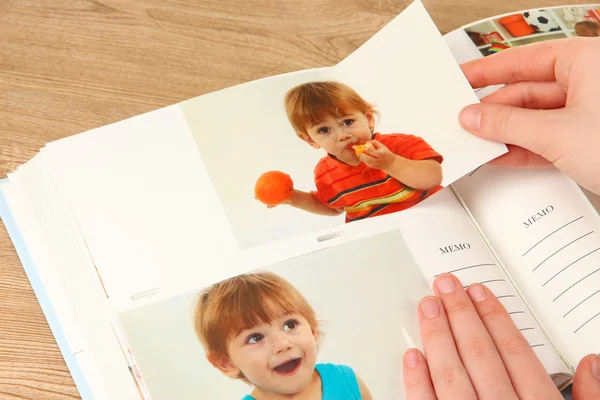 Photos in hands and photo album on wooden table — Stock Photo, Image