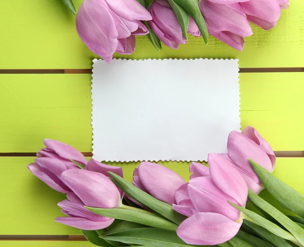 束美丽的紫色郁金香和空白卡上绿色木质背景 — 图库照片
