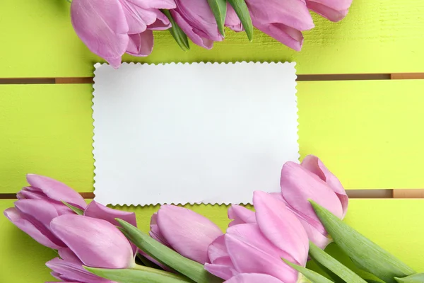 Hermoso ramo de tulipanes morados y tarjeta en blanco sobre fondo de madera verde —  Fotos de Stock