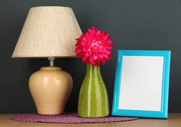 Moldura de foto colorida, lâmpada e flores na mesa de madeira no fundo cinza — Fotografia de Stock
