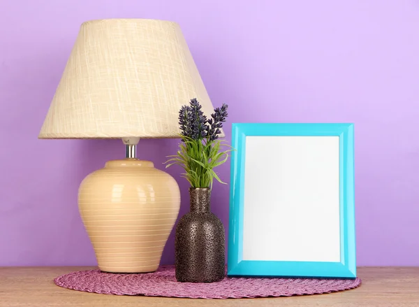 Colorful photo frame, lamp and flowers on wooden table on lilac background — Stock Photo, Image