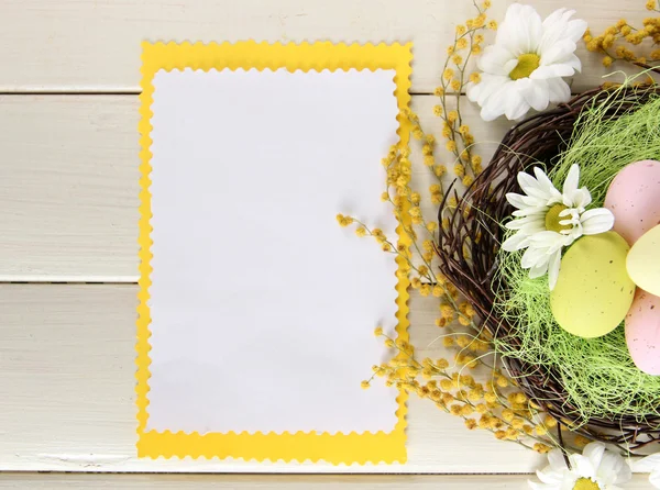 Lege kaart met Pasen eieren en mimosa bloemen, op witte houten achtergrond — Stockfoto