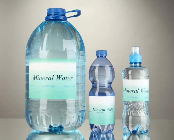 Diferentes botellas de agua con etiqueta sobre fondo gris —  Fotos de Stock
