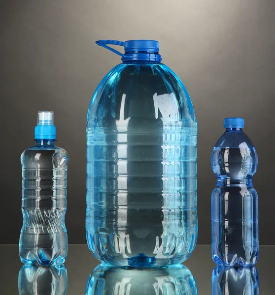 Різні пляшки води на сірому фоні — стокове фото