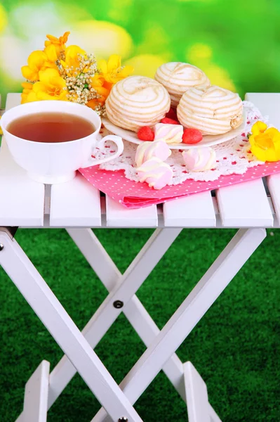 Beautiful composition with cup of tea and marshmallow on wooden picnic table on natural background — Stock Photo, Image