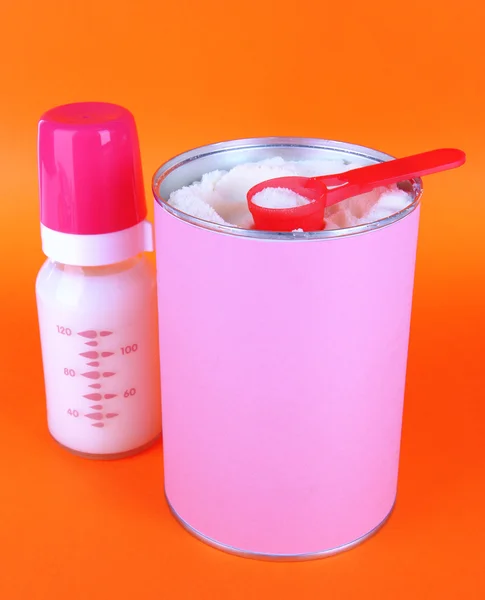 Powdered milk with baby bottle of milk on orange background