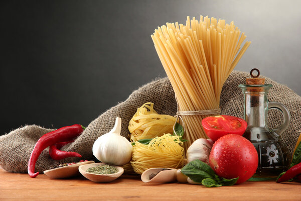Pasta spaghetti, vegetables and spices, on wooden table, on grey background