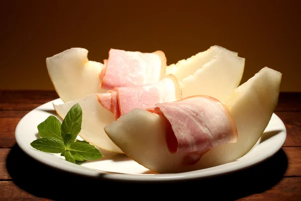 Jambon et melon de parme, sur table en bois, sur fond jaune — Photo