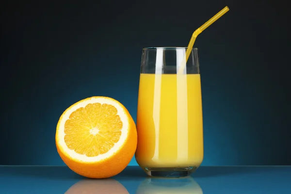 Köstlicher Orangensaft im Glas und daneben Orange auf dunkelblauem Hintergrund — Stockfoto