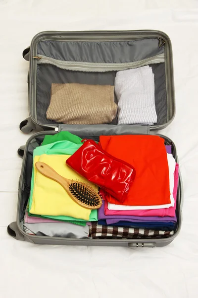 Valise ouverte grise avec vêtements sur le lit — Photo