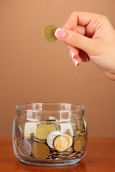 Opslaan, vrouwelijke hand een munt ingebruikneming glazen fles, op een achtergrond met kleur — Stockfoto