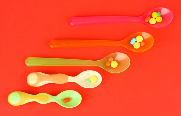 Plastic spoons with color pills on red background — Stock Photo, Image