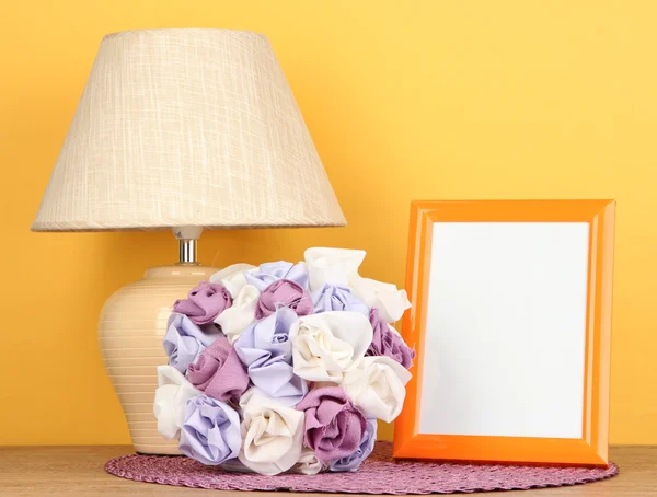 Marco de fotos colorido, lámpara y flores en la mesa de madera sobre fondo amarillo — Foto de Stock