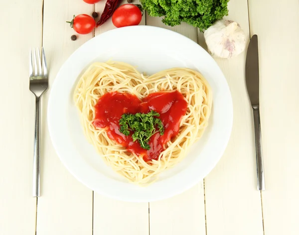 Cooked spaghetti carefully arranged in heart shape and topped with tomato sauce, on wooden background — Stock Photo, Image