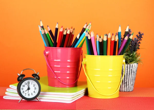 Kleurrijke potloden in twee emmers met copybooks op tafel op oranje achtergrond — Stockfoto