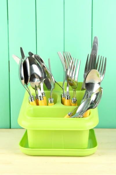 Knives, spoons, forks in plastic container for drying, on color wooden background — Stock Photo, Image