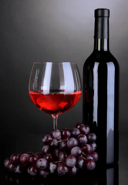 Sklenice na červené víno a láhev vína na šedém pozadí — Stock fotografie